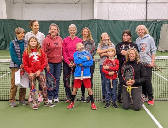New Circle Mentors and mentees gathered for group photograph at Middlebury Indoor Tennis. Everyone is holing a tennis racket.